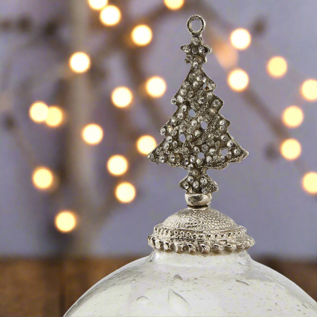 Decorative glass Christmas bauble hanging ornament with a bejewelled silver tree-shaped top. festive scene.