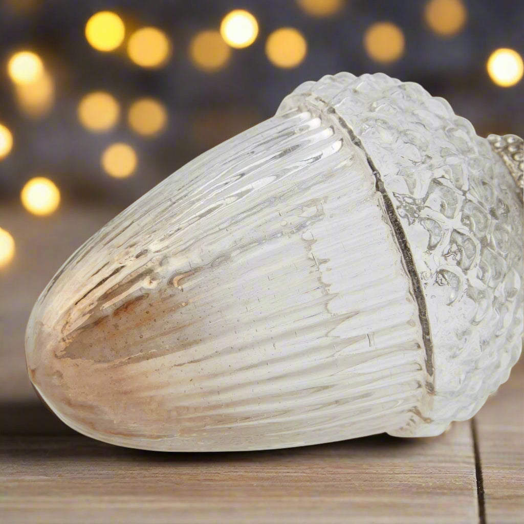 Decorative festive hanging glass acorn with ombre colouring and intricate design laying on a wooden table with festive background.
