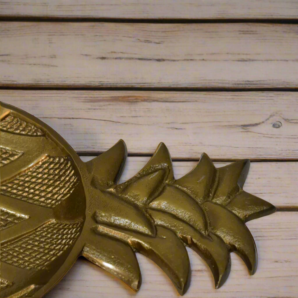 Close-up of the leafy top section of the antique pineapple dish, revealing its detailed texture and brass finish on a wooden background.