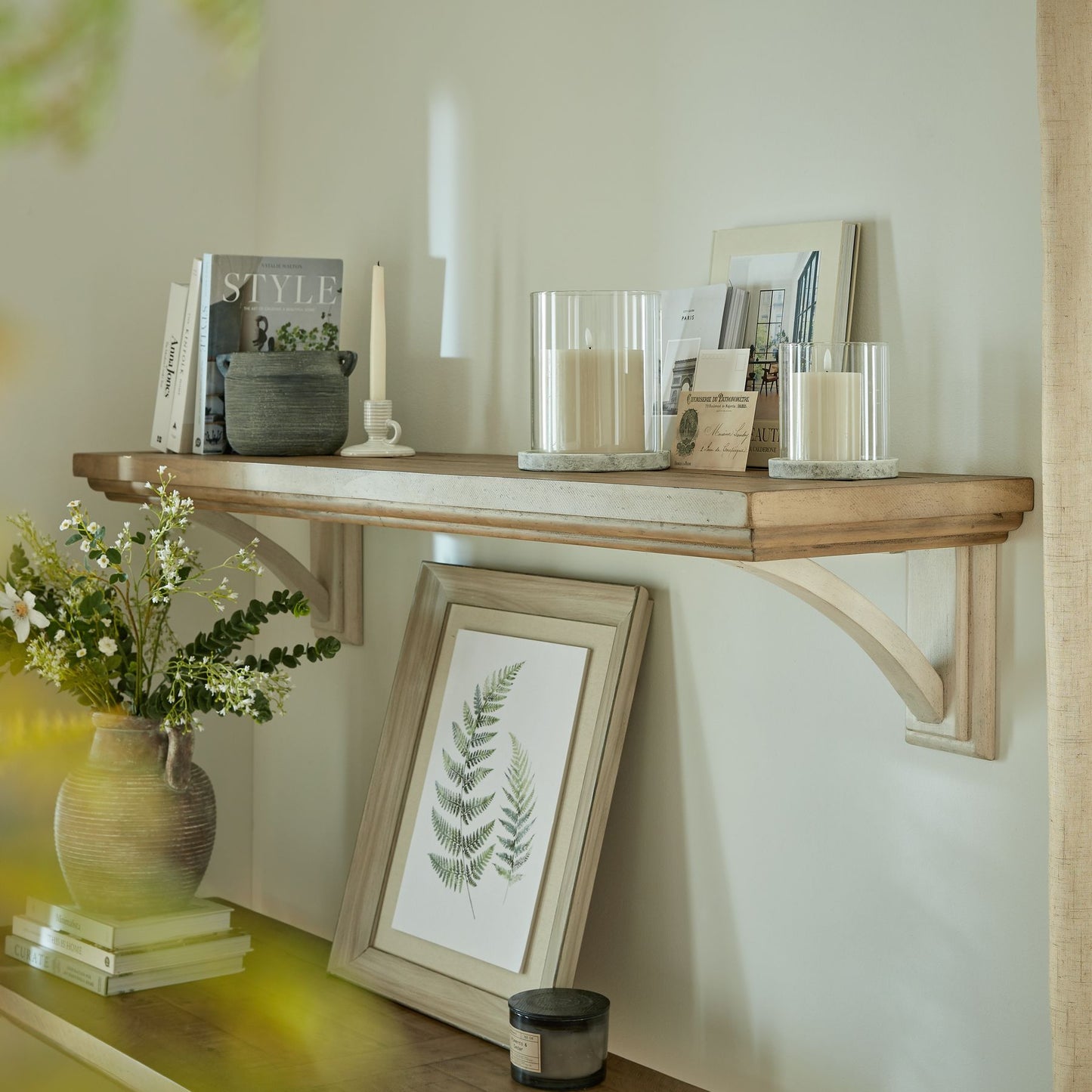 Large and small Athena Stone hurricane lanterns styled on a shelf with other home décor items.