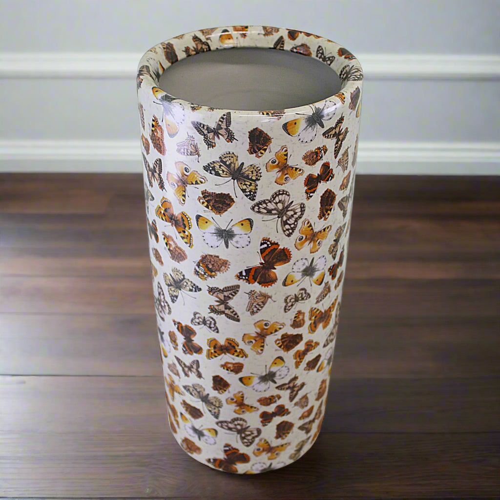 Angled image of glazed ceramic umbrella stand with brown-speckled butterfly print, styled on light wood flooring – Purple Flamingo UK
