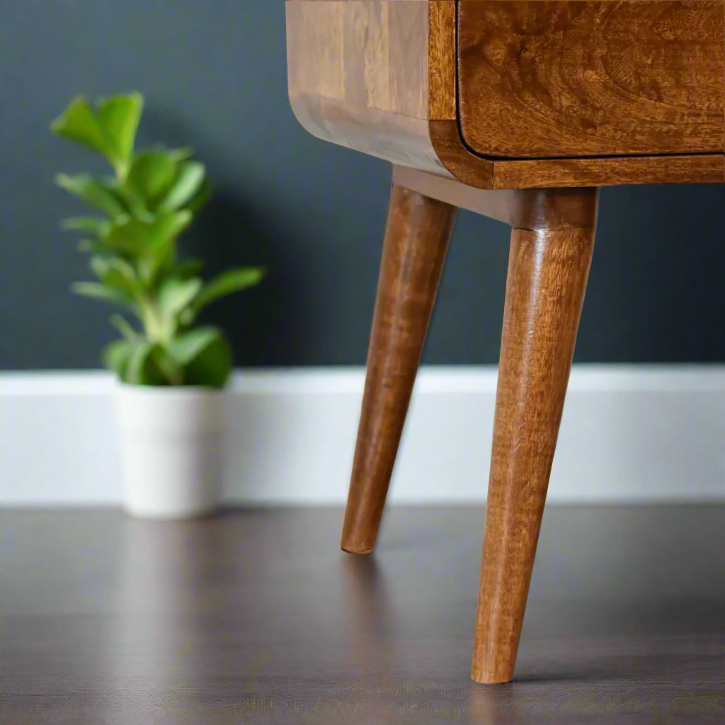 Close-up of the tapered Nordic-style wooden legs of the curved chestnut bedside table, showing the smooth wood finish against a subtle background.