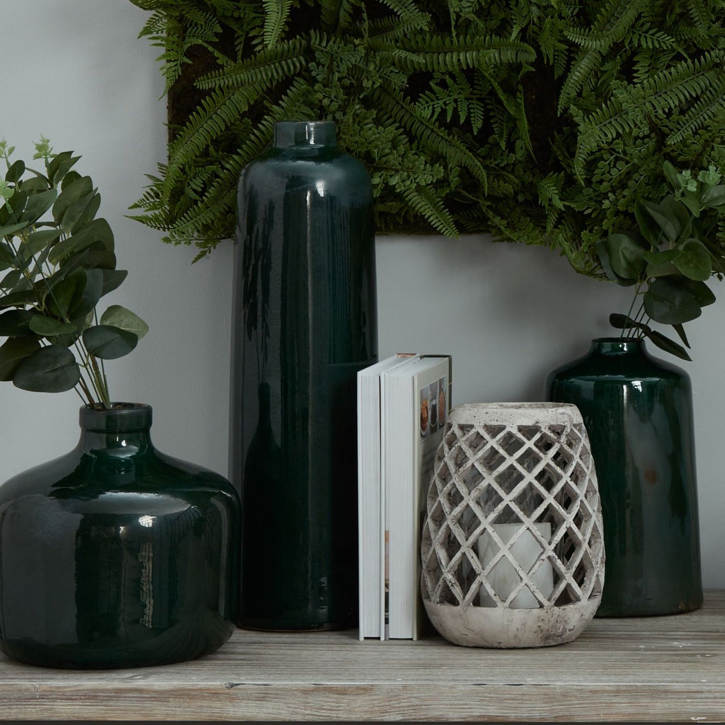 Ceramic lattice lantern lit with a candle, styled with ornamental plants in black vases of different heights.