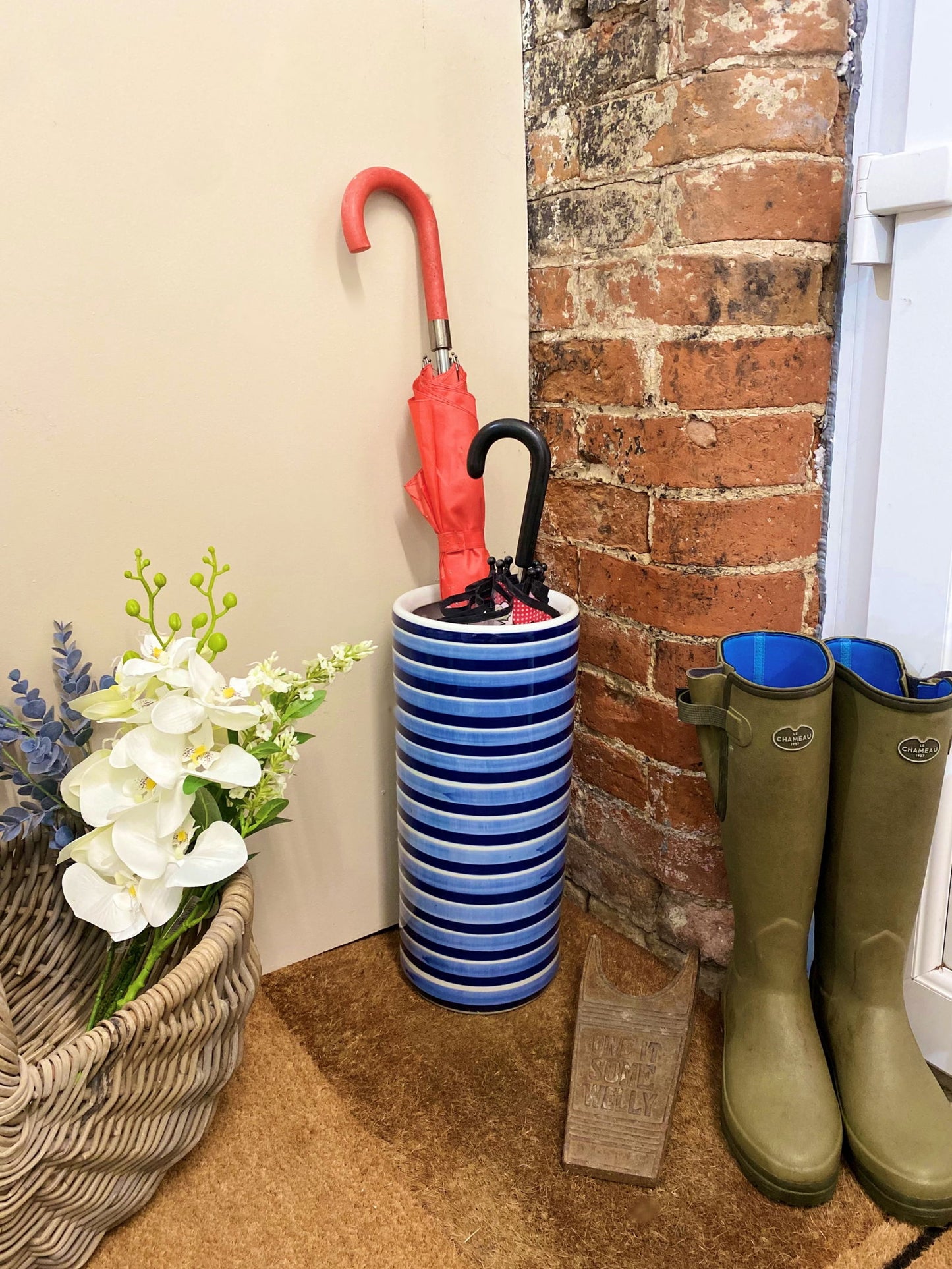 Purple Flamingo blue and white striped ceramic umbrella stand holding two umbrellas, perfect for a tidy hallway.