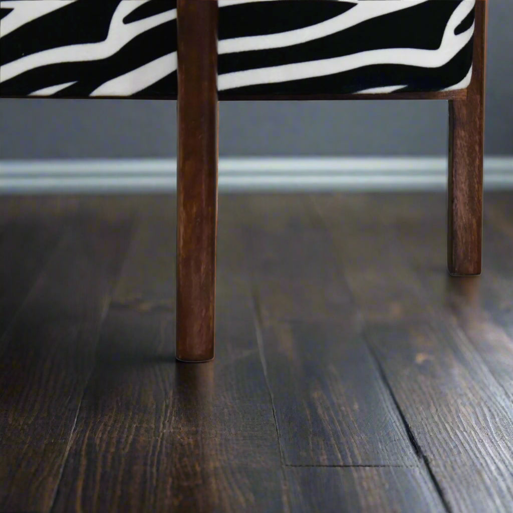 Zebra print footstool with walnut legs styled in a room setting with neutral flooring.