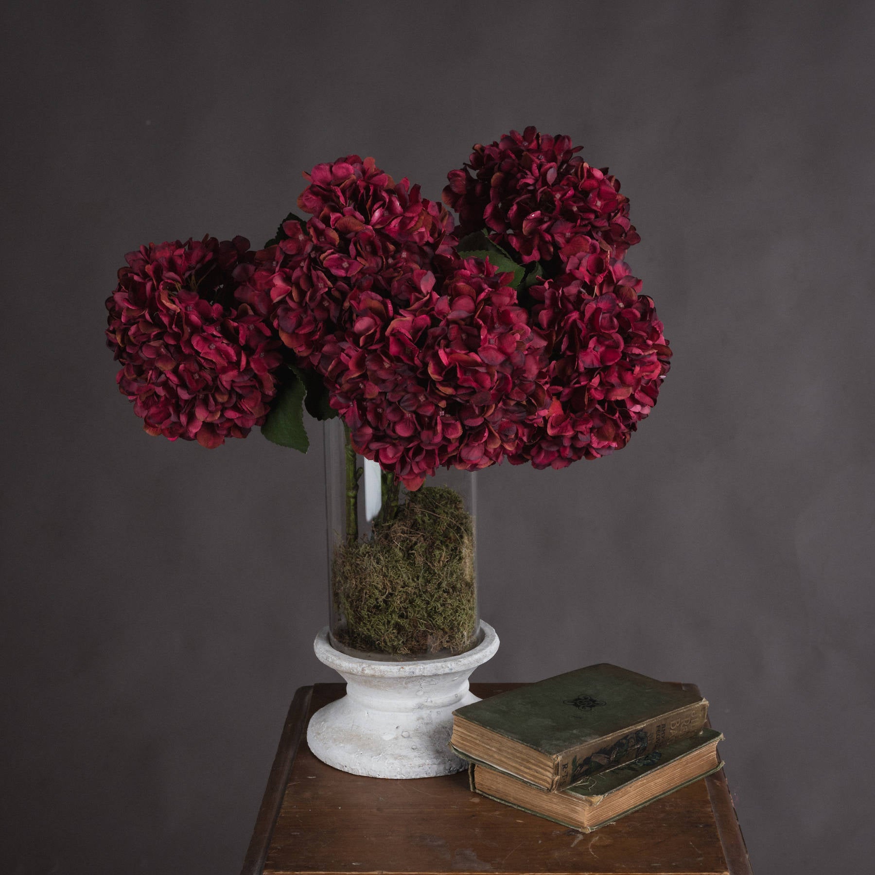 A beautiful arrangement of vibrant autumn Ruby hydrangeas in a glass vase with moss on a wooden table.