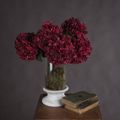 A beautiful arrangement of vibrant autumn Ruby hydrangeas in a glass vase with moss on a wooden table.