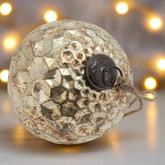 Round glass bauble placed on a wooden table showing close up detailed of brown bauble cap, the burnished glass honeycomb textured design and attached hanging twine.