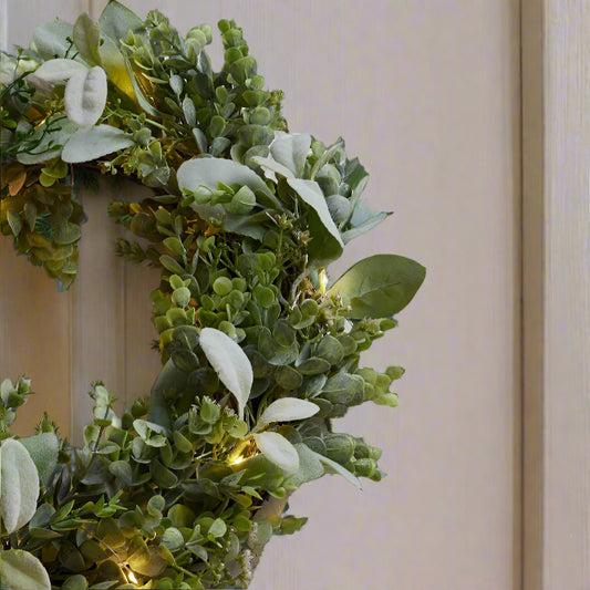 Beautiful natural looking Eucalyptus and Lambs Ear wreath hung from a cream front door and lit by its built in LED lights