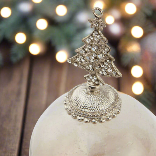 Decorative glass hanging Christmas ornament with a silver bejewelled tree on top. Festive scene.