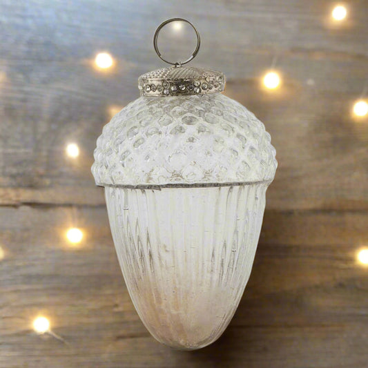 Decorative glass ombre colour acorn-shaped hanging christmas bauble with textured surface and metallic top adorned in decorative stones laying on a wooden table