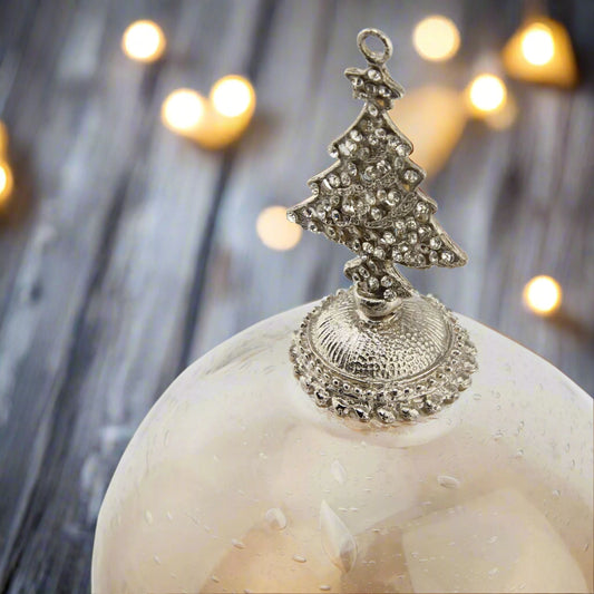 Large Decorative Christmas Glass Bauble ornament with a bejewelled silver tree top on a wooden table with fairy lights