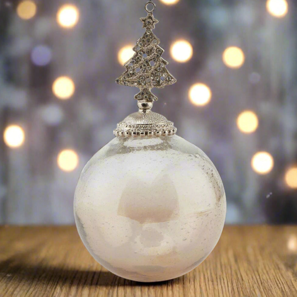 Decorative glass Christmas hanging ornament with an ombre coffee coloured bauble ball and tree-shaped bejewelled top placed on a wooden table with festive background.