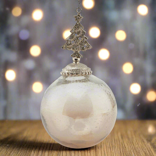 Decorative glass Christmas hanging ornament with an ombre coffee coloured bauble ball and tree-shaped bejewelled top placed on a wooden table with festive background.