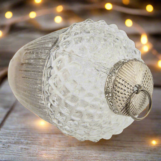 Glass hanging acorn decoration with textured surface and metallic cap with decorative stones. Festive scene.