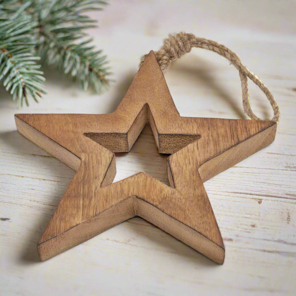 Wooden star hanging decoration placed on a table showcasing close up view of cut-out star shape in middle and hanging twine. Buy at Purple Flamingo UK