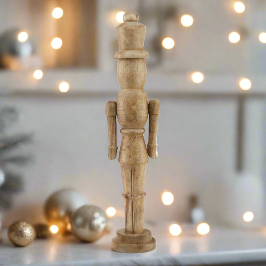 wooden nutcracker figure placed on a white marble shelf, surrounded by festive coffee and cream coloured baubles and fairy lights.