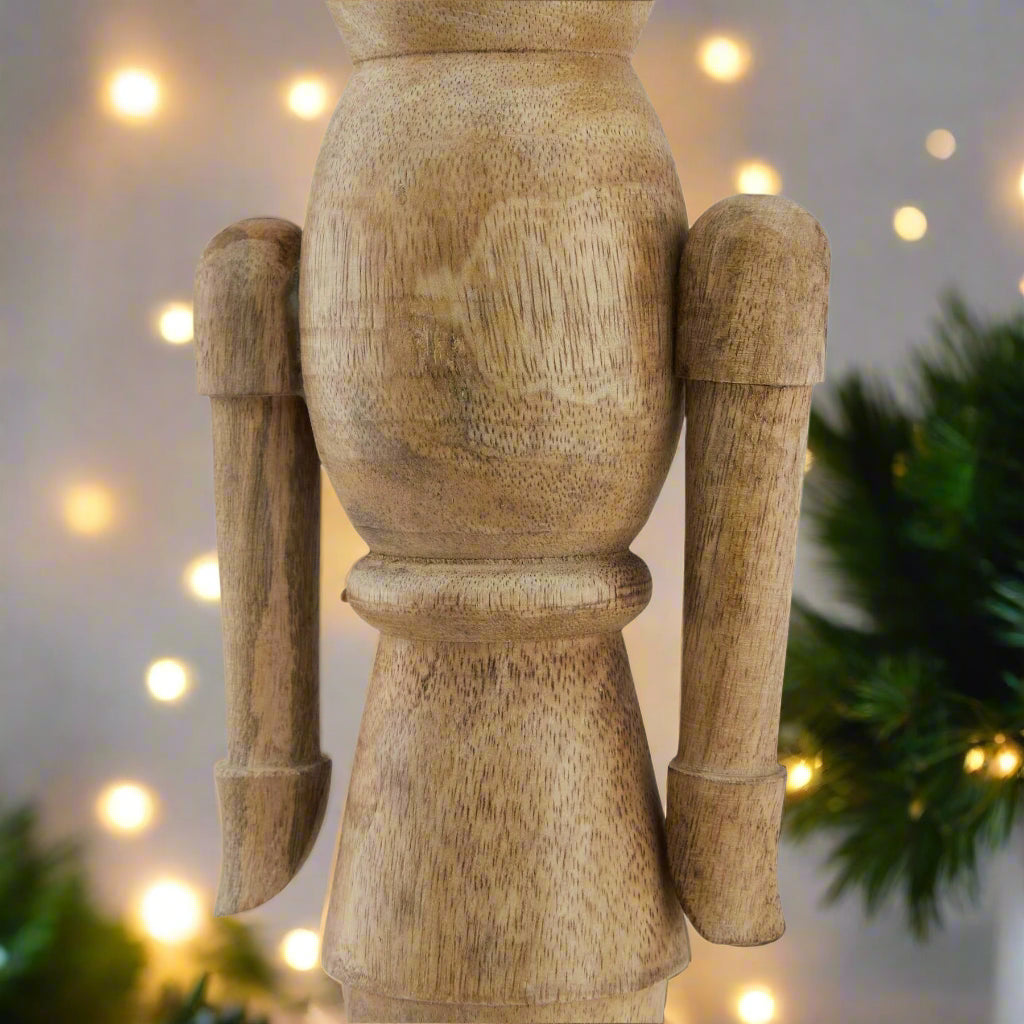 Close up view of middle section of wooden nutcracker figure showcasing the arms and smooth crafted curves of the ornament, setting is festive. Purchase at Purple Flamingo UK.