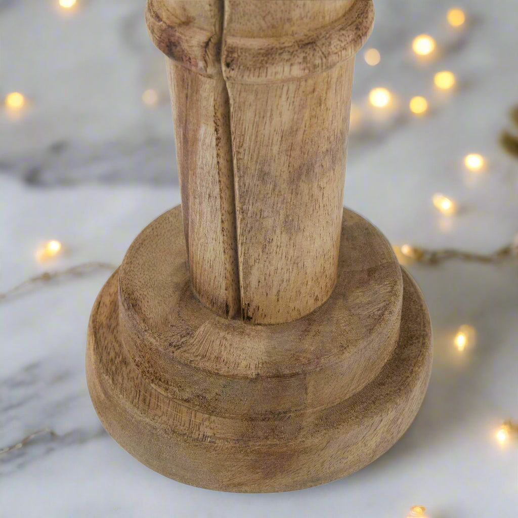 Close up view of bottom section of wooden nutcracker figure showcasing the rounded sturdy base and quality wood, setting is festive. Purchase at Purple Flamingo UK.