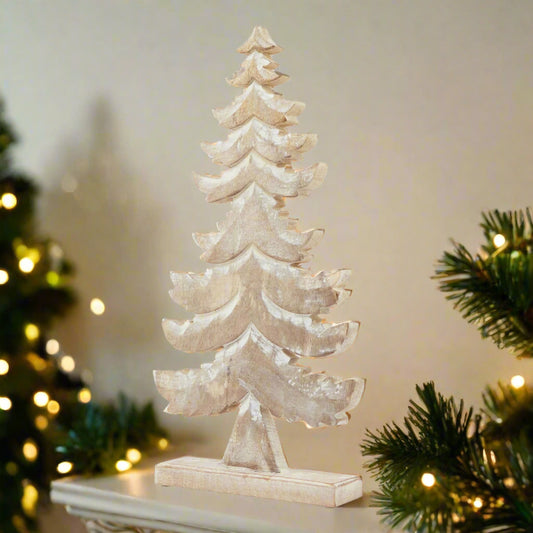 Decorative tiered wooden Christmas tree decoration with white wash snowy effect, placed on a cream mantle flanked by green garlands and Christmas tree bedecked with warm fairy lights. 