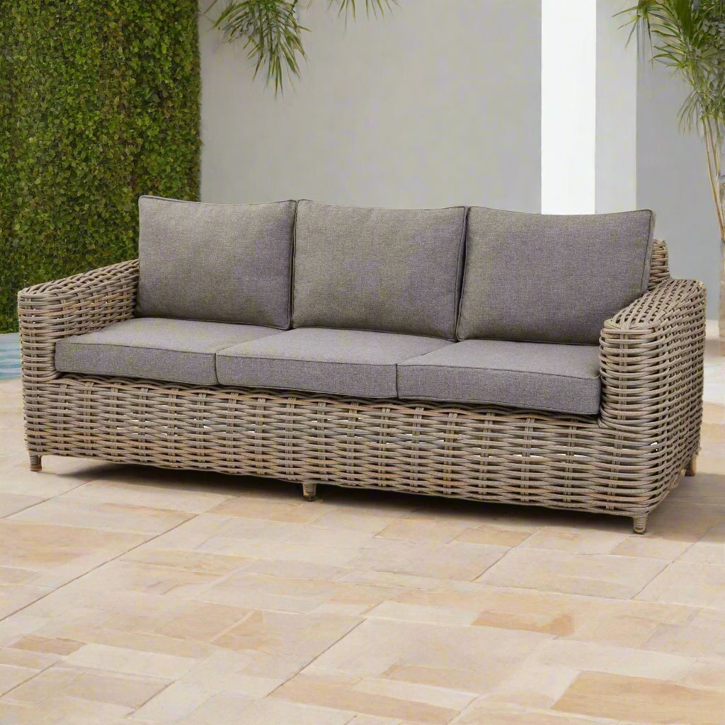 Front view of the Amalfi three-seater sofa, showing the Olefin cushions, wicker weave, and acacia feet in an ample outdoor space.