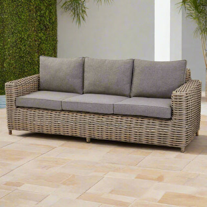 Front view of the Amalfi three-seater sofa, showing the Olefin cushions, wicker weave, and acacia feet in an ample outdoor space.
