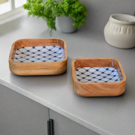 Top-down view of the blue and white square bowls on a countertop, showing more of their intricate internal design, with a white jug and ornamental flower in the background.