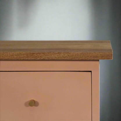 A closer look at the left edge of the blush pink hand-painted bedside table, focusing on the shiny drawer knob and the upper wooden surface.