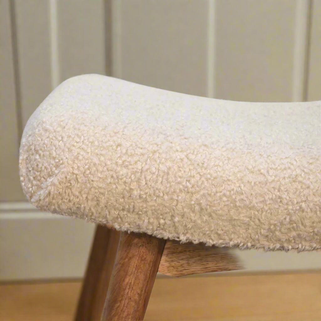 Close-up focus on the right edge of the Boucle Cream Curve Stool's upholstered woven seat and a section of its supporting legs.