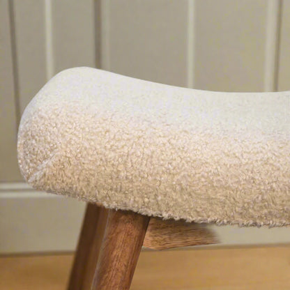 Close-up focus on the right edge of the Boucle Cream Curve Stool's upholstered woven seat and a section of its supporting legs.