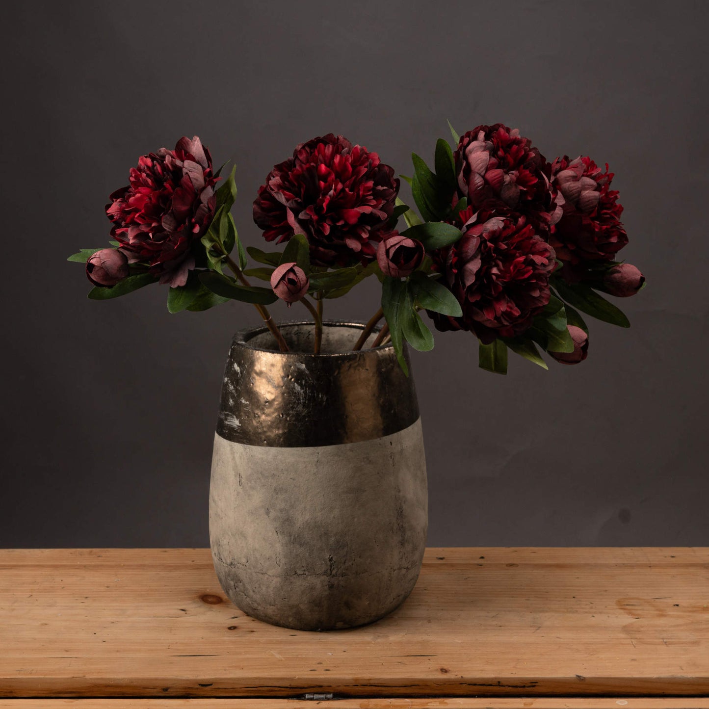 Front view of three burgundy peony roses in a vase on a wooden surface.