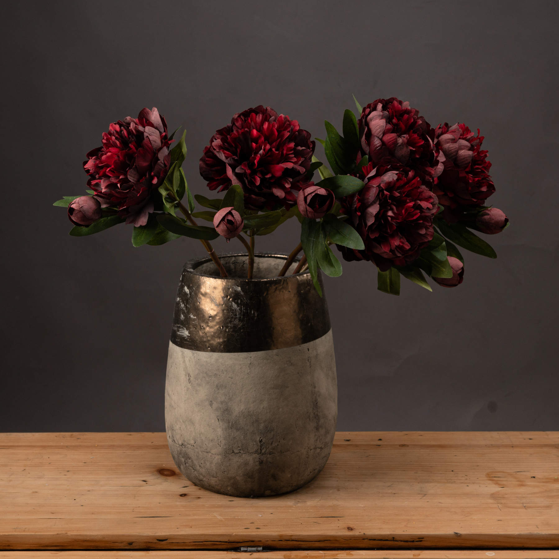Front view of three burgundy peony roses in a vase on a wooden surface.