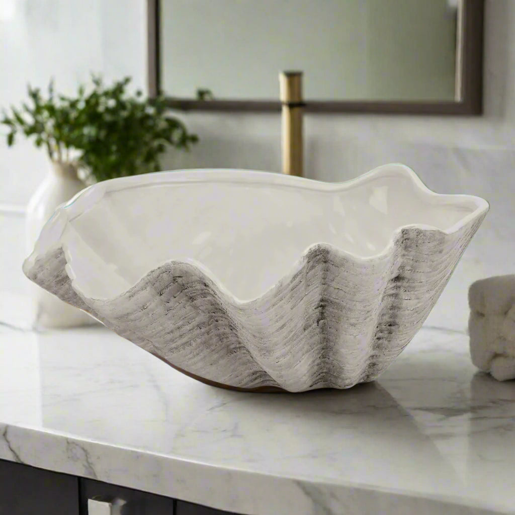 Front view of the large 40cm ceramic Adele Shell bowl on a white tabletop, with an ornamental flower positioned behind it.