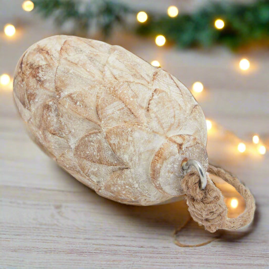 Close up view of intricately carved wooden pine cone decoration with a twine rope attachment laying on a festive table.