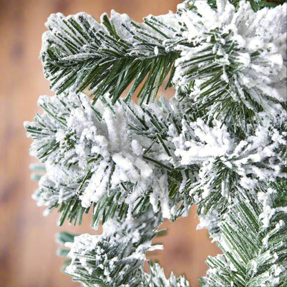 Close-up of the realistic snow-dusted needles and branches of an extra large artificial snowy spruce Christmas tree.
