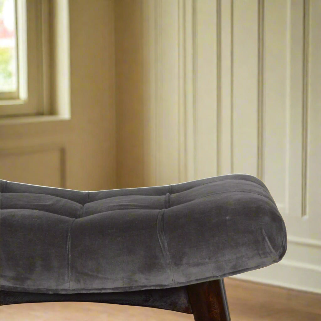 Close view of the left edge of the grey velvet curve stool's seat, showing the soft grey velvet fabric in detail.