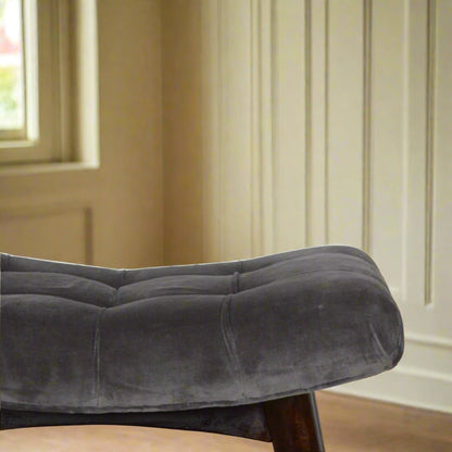 Close view of the left edge of the grey velvet curve stool's seat, showing the soft grey velvet fabric in detail.