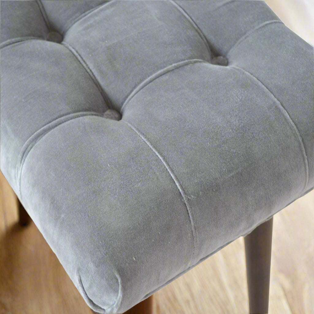Top-down focus on the elegant deep button pattern on the upholstered seat of the grey velvet curve stool.