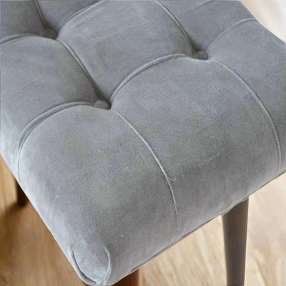Top-down focus on the elegant deep button pattern on the upholstered seat of the grey velvet curve stool.