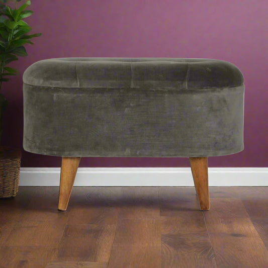 Front view of the Grey Velvet Storage Footstool with an oak-ish finish, upholstered in grey velvet, positioned beside an indoor plant.