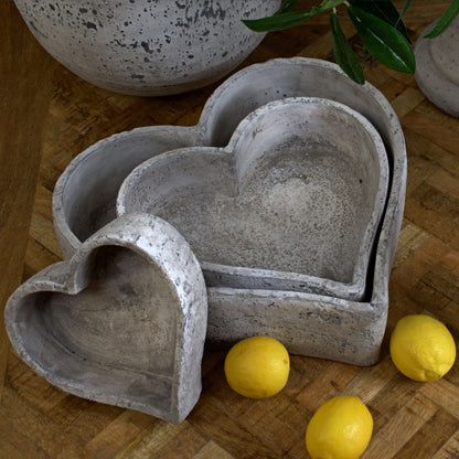 Set of three graduated heart-shaped ceramic dishes with a rustic stone finish, styled with lemons and greenery for a fresh decor look.
