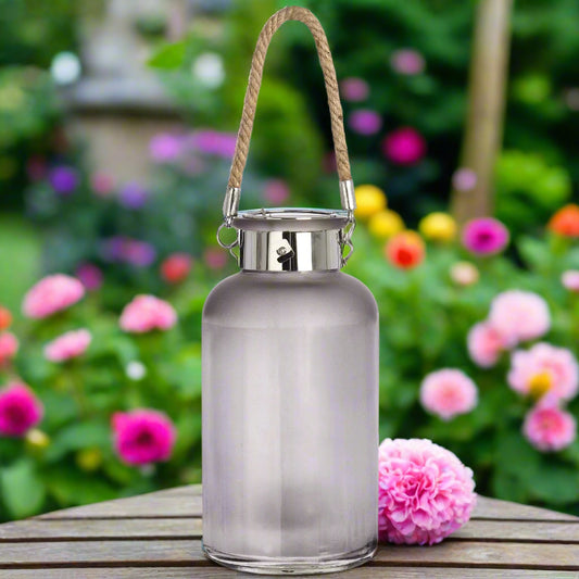 Lantern placed outdoors among flowers with visible rope handle for hanging.
