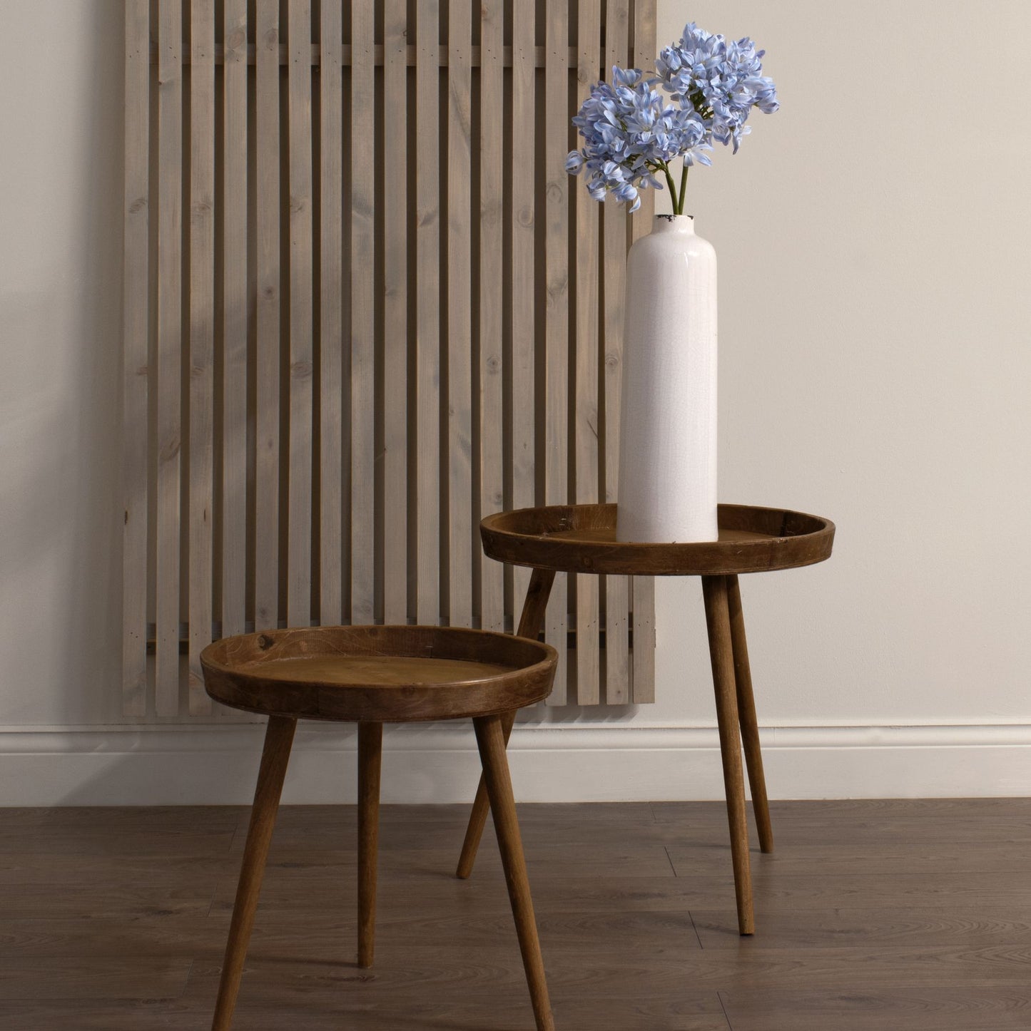 Light blue agapanthus arranged in a white vase on a table with a stool beside it.