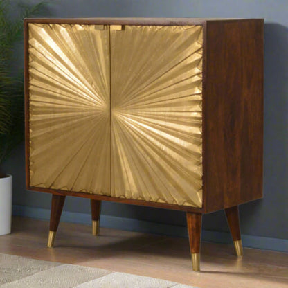 Angled front view of the Manila Gold Cupboard in a room setting, showcasing its striking brass-plated sunburst doors and solid mango wood chestnut finish.
