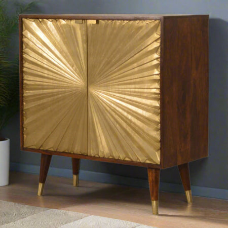 Angled front view of the Manila Gold Cupboard in a room setting, showcasing its striking brass-plated sunburst doors and solid mango wood chestnut finish.