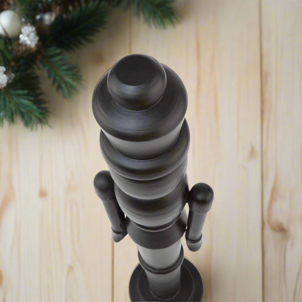 Close-up of the sculpted head and crown of a minimalist black wooden large nutcracker decoration.