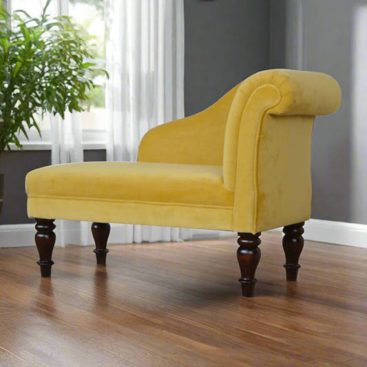 Angled view from the backrest side of the mustard velvet chaise, highlighting its curved backrest and all turned legs, with an inhouse plant in the background.