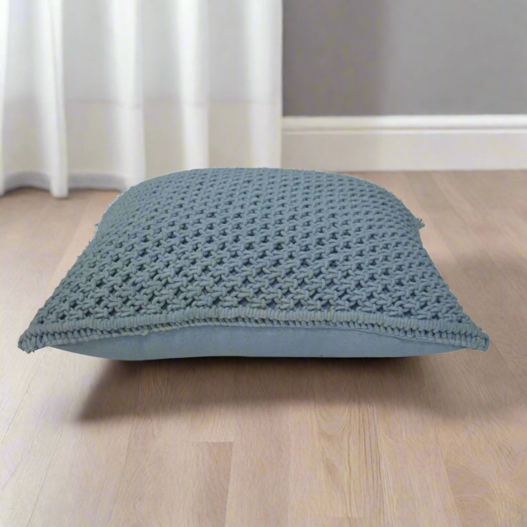 Side view of a Myra blue cushion placed horizontally on a table, illustrating the generous size and plumpness of its filling.