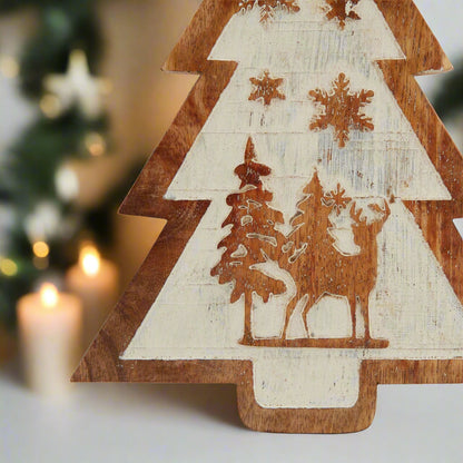 Close-up of the intricate carved snow scene on a natural wooden tree decoration, showing reindeer and frosted trees.