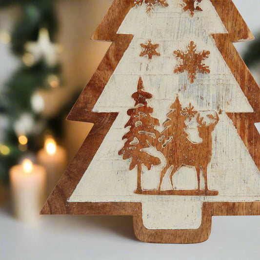Close-up of the intricate carved snow scene on a natural wooden tree decoration, showing reindeer and frosted trees.
